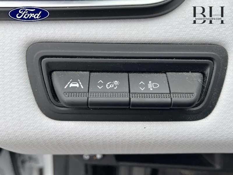 Gros plan sur les boutons de réglage d'assistance à la conduite et d'éclairage sur tableau de bord blanc d'une Renault Clio blanche.