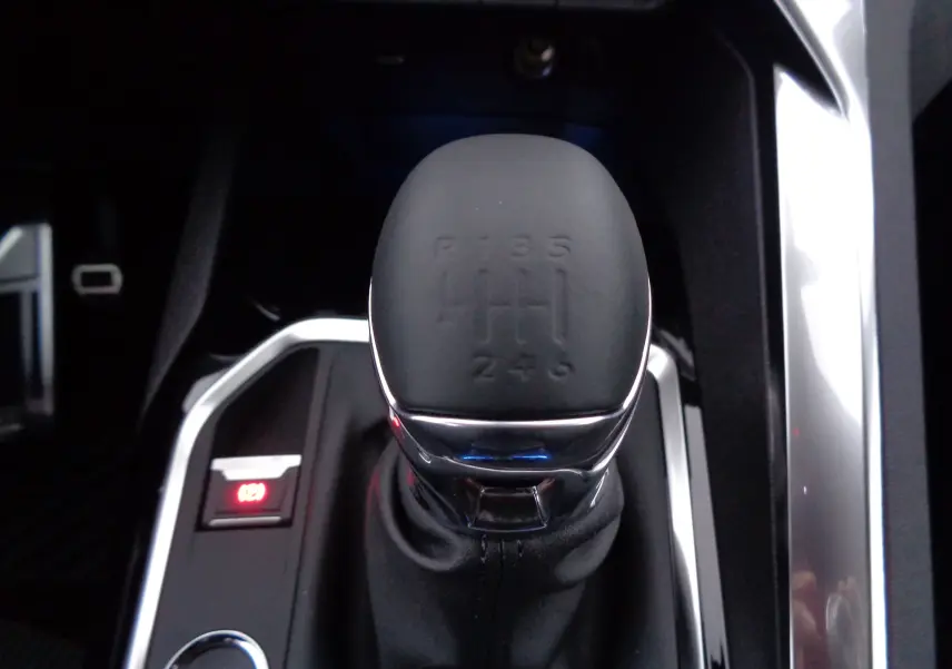 Le levier de vitesses manuel noir du Peugeot 5008 GT 2023 vu de dessus avec contour chromé et frein à main électronique.