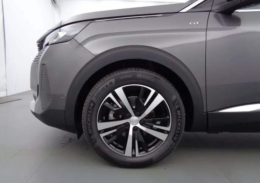 Gros plan sur la roue avant gauche du Peugeot 5008 gris platinium métal avec badge GT visible sur l'aile.