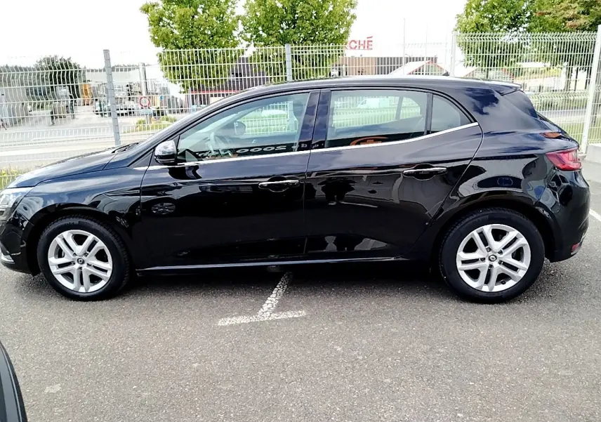 Profil côté gauche d'une Renault Mégane IV Business noire, garée sur un parking extérieur, roues alliage visibles.