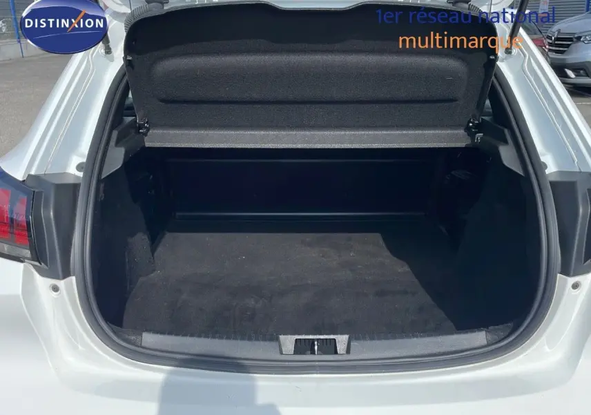 Coffre ouvert d'une Peugeot 208 blanc banquise vue arrière, montrant l'espace de chargement vide et propre.