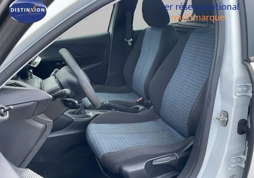 Intérieur côté gauche d'une Peugeot 208 blanc banquise 2021, sièges tissu bleu et noir, volant et levier de vitesse manuels visibles.