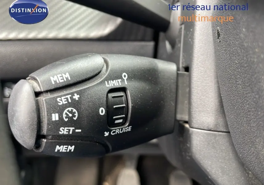 Gros plan sur la commande de régulateur de vitesse noire dans l'habitacle d'une Peugeot 208 blanche banquise.