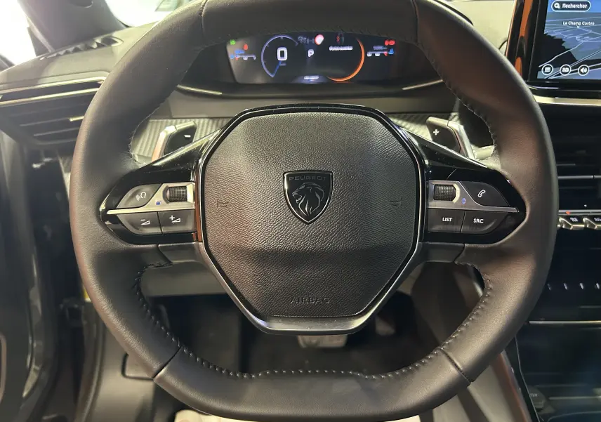 Vue rapprochée du volant cuir noir du Peugeot 2008 II Ph.2 Allure Hybrid avec commandes intégrées et tableau de bord numérique.