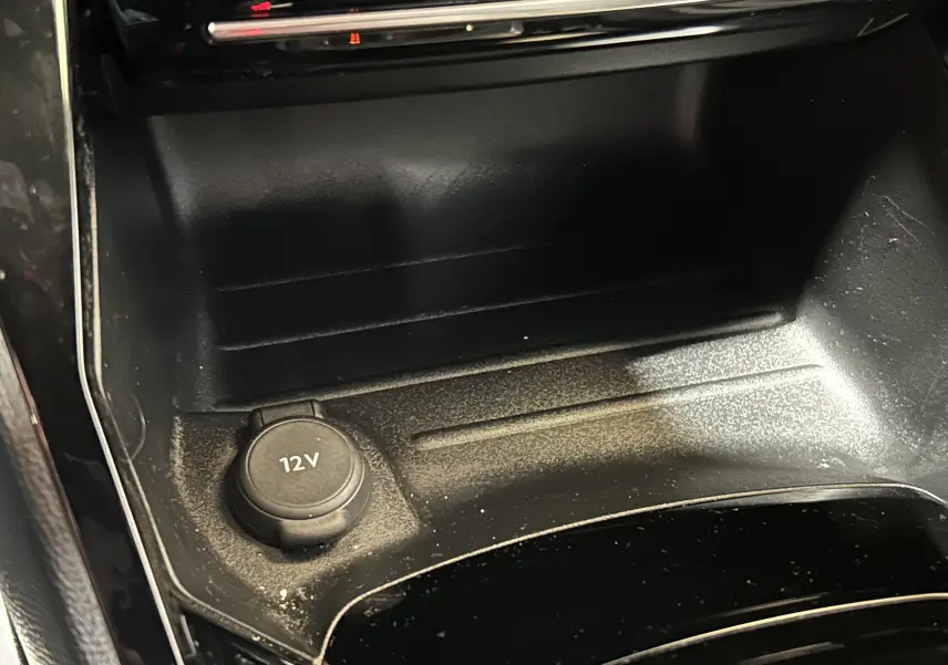 Gros plan sur la prise 12V dans la console centrale noire du Peugeot 2008 II Ph.2 Allure Hybrid 145 gris Selenium.