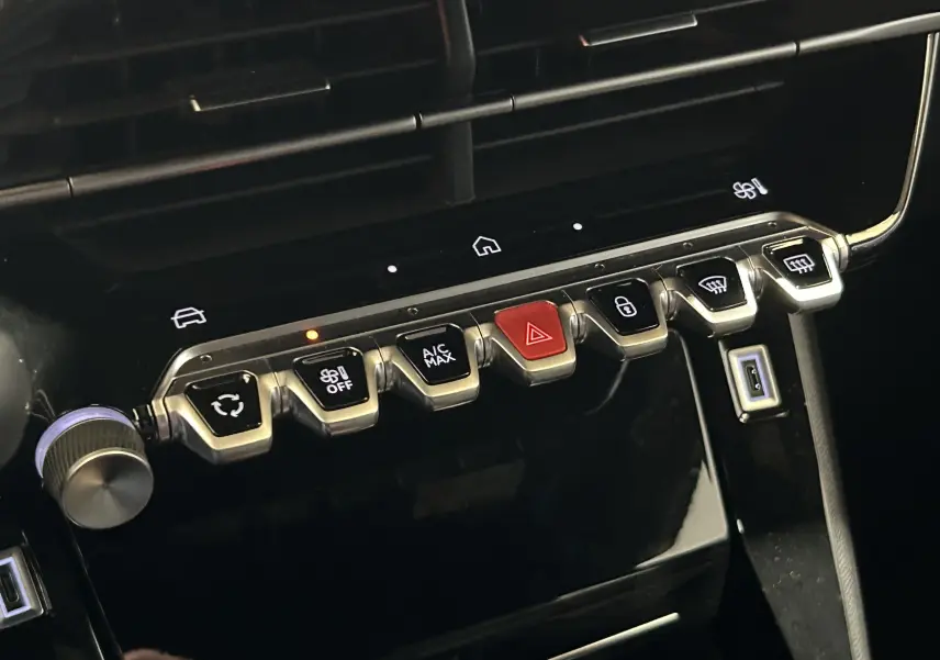 Gros plan sur la rangée de boutons de commande du tableau de bord du Peugeot 2008 gris, avec bouton rouge d’alerte au centre.