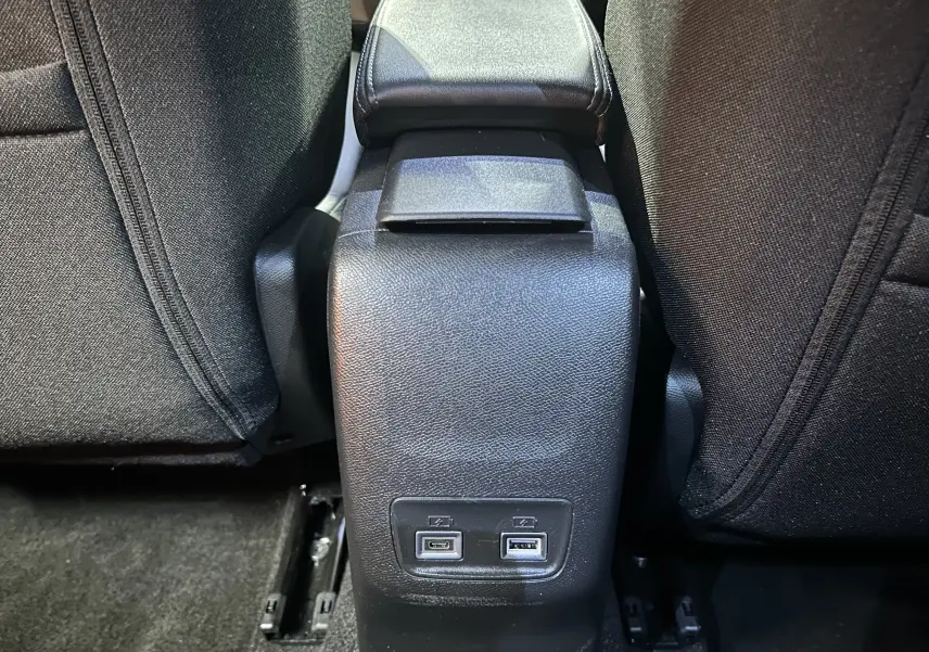 Vue rapprochée du port USB arrière entre les sièges noirs du Peugeot 2008 II Ph.2 Allure Hybrid 145 gris Selenium.