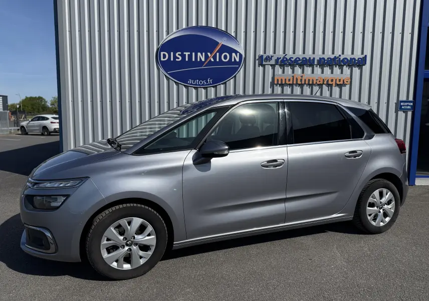 Vue de profil côté gauche d'une Citroën C4 Picasso gris métallisé garée devant un bâtiment avec enseigne Distinxion.
