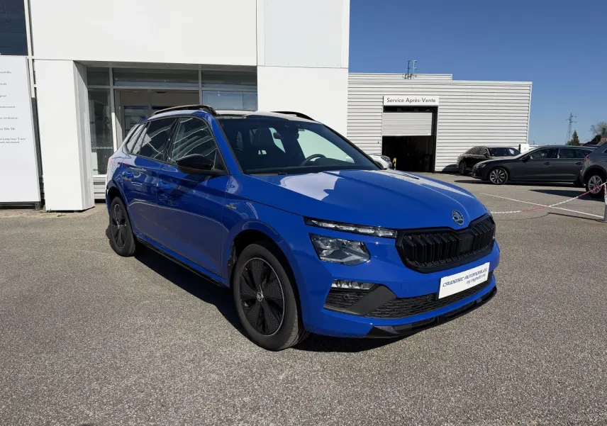 Vue 3/4 avant d'un Skoda Kamiq bleu avec calandre noire et jantes alliage noires sur parking extérieur.