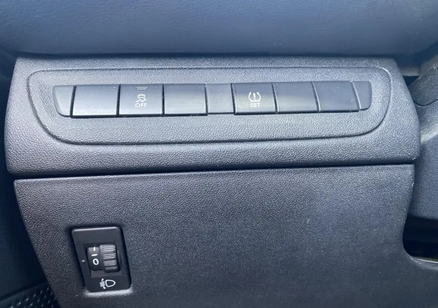 Gros plan sur les commandes de contrôle de stabilité et réglage des phares dans l'habitacle d'une Peugeot 208 gris foncé 2018.