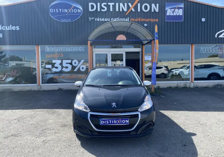 Peugeot 208 gris foncé vue de face, stationnée devant un concessionnaire Distinxion avec enseigne visible.