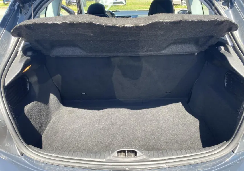 Coffre ouvert d'une Peugeot 208 gris foncé vue de l'arrière, montrant l'espace de chargement vide et la tablette cache-bagages relevée.