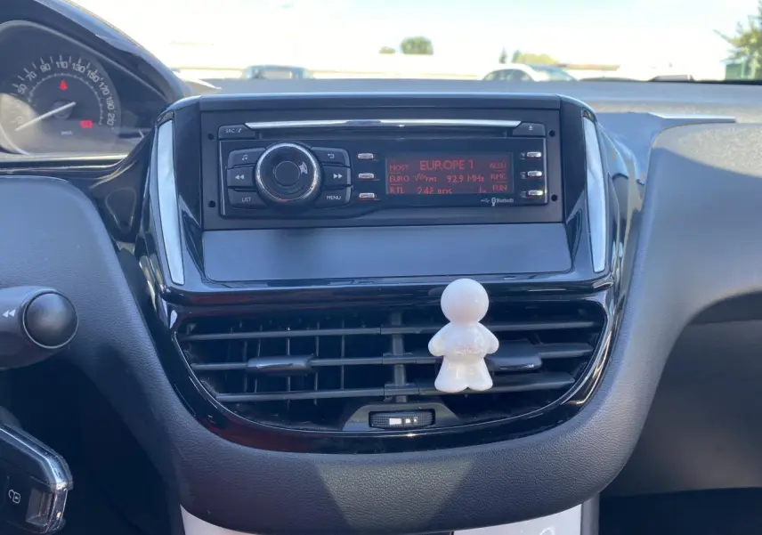 Tableau de bord central d'une Peugeot 208 gris foncé 2018 avec autoradio et petite figurine blanche sur la grille d'aération.