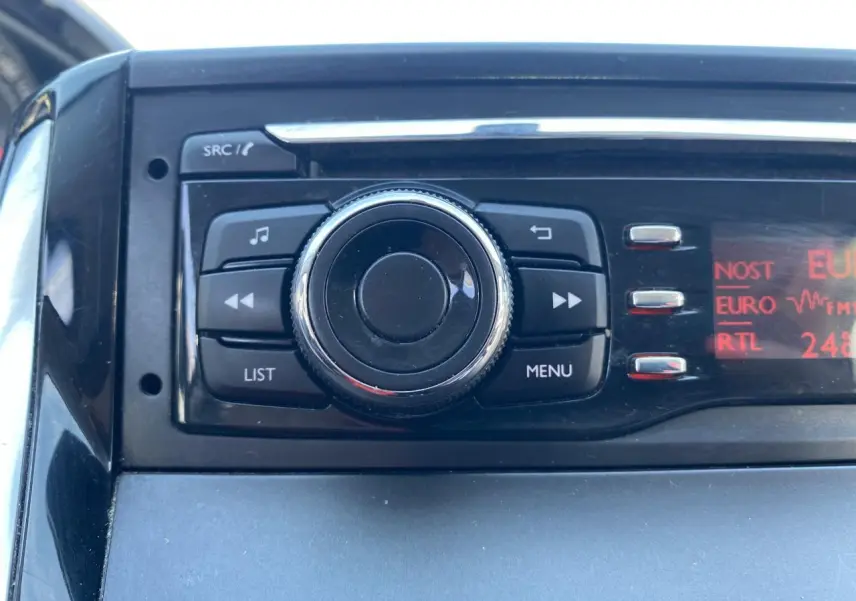 Gros plan sur la commande centrale de l'autoradio avec écran rouge dans l'habitacle d'une Peugeot 208 gris foncé.
