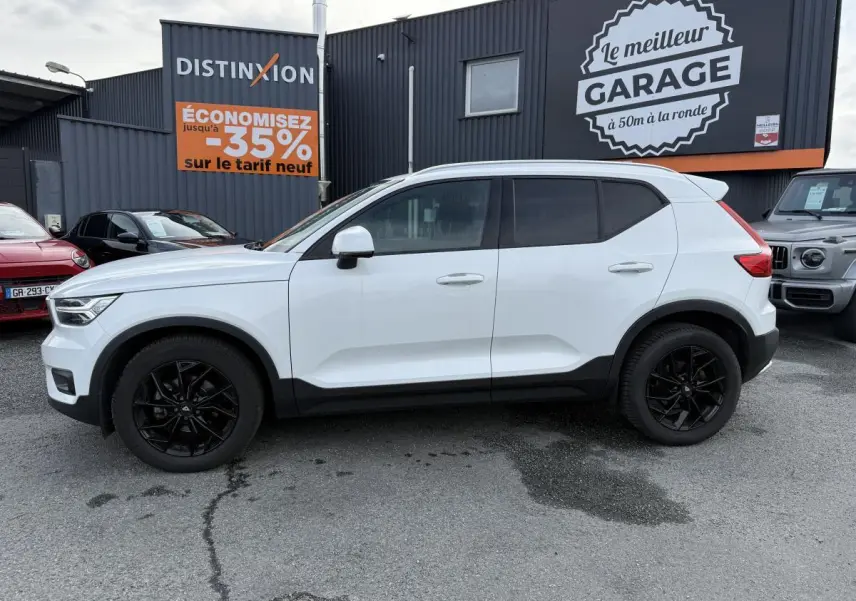 Profil côté gauche d'un Volvo XC40 blanc avec jantes alliage noires, garé devant un garage commercial.