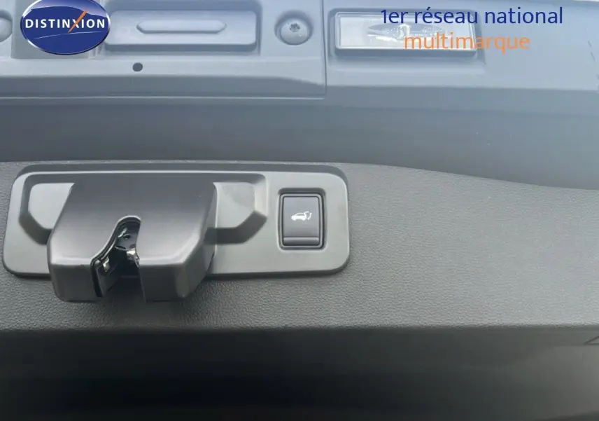 Gros plan sur la serrure et le bouton d'ouverture électrique du hayon d'une Renault Symbioz blanc nacré.