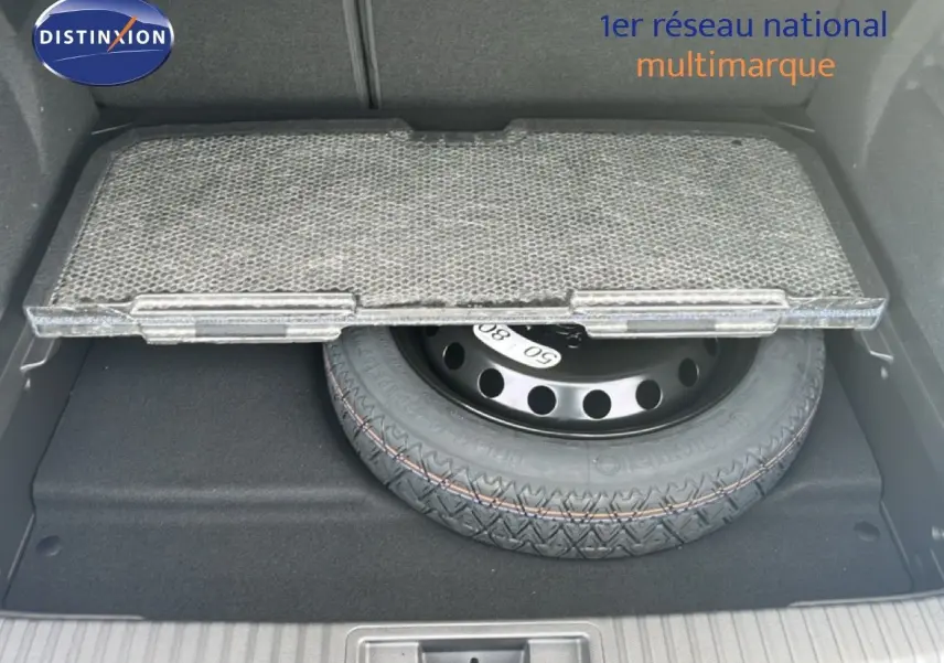 Coffre ouvert montrant la roue de secours sous un tapis partiellement relevé, intérieur noir du Renault Symbioz blanc nacré.