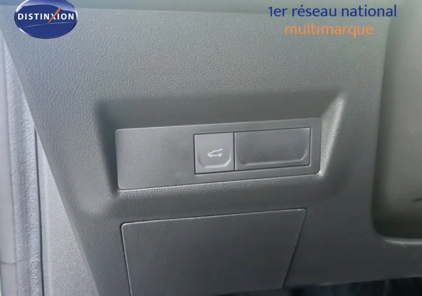 Bouton d'ouverture du coffre sur panneau intérieur noir d'une Renault Symbioz blanche nacrée, vue rapprochée.