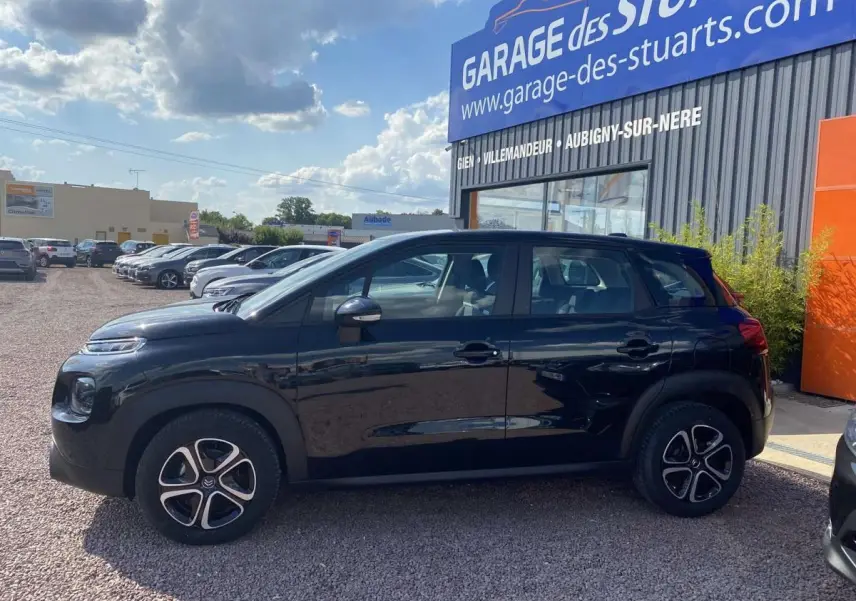 Profil côté gauche d'un Citroën C3 Aircross noir 2021, version Shine, stationné devant un garage avec jantes distinctives.