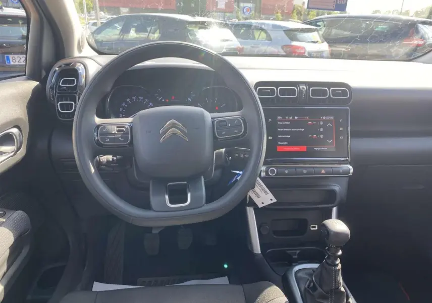 Vue intérieure frontale du tableau de bord noir du Citroën C3 Aircross 2021 avec volant, écran tactile et levier de vitesse manuel.