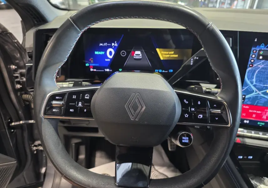 Vue rapprochée du volant Alcantara noir avec surpiqûres bleues du Renault Austral 2024, tableau de bord numérique en arrière-plan.