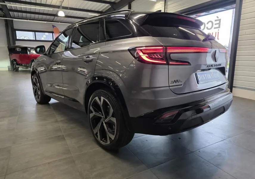 Vue 3/4 arrière droite d'un Renault Austral gris foncé avec jantes alliage 20 pouces et toit noir étoilé en intérieur showroom.
