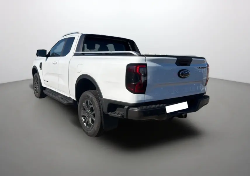Ford Ranger Wildtrak blanc pur vu en 3/4 arrière gauche avec arceau sport et barres de toit visibles.
