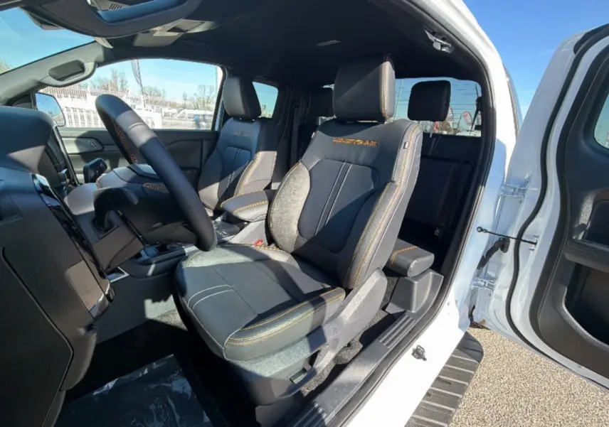 Vue intérieure côté conducteur du Ford Ranger blanc pur 2025, sièges noirs avec surpiqûres orange Wildtrak visibles.