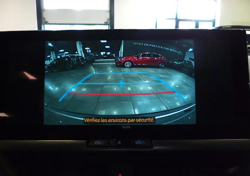 Vue caméra de recul montrant un Toyota C-HR hybride gris minéral en intérieur, avec lignes de guidage bleues et rouges.