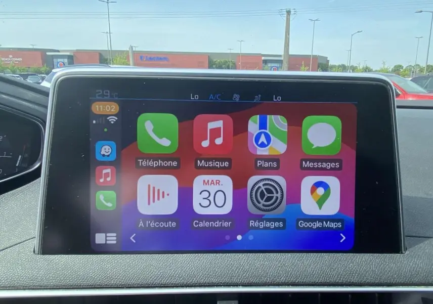 Écran tactile central du Peugeot 3008 blanc 2018 affichant les applications Apple CarPlay en plein jour.