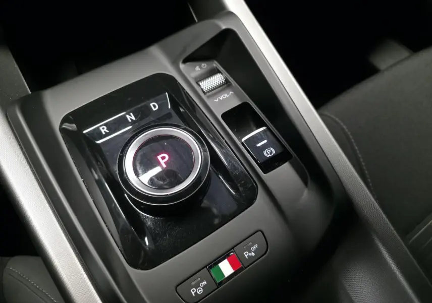 Gros plan sur la console centrale noire de l'Alfa Romeo Tonale bleu, avec sélecteur de vitesse rotatif et drapeau italien.