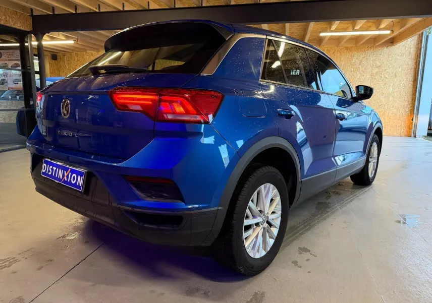 Vue 3/4 arrière droite d'un Volkswagen T-Roc bleu avec feux arrière LED et jantes alliage en intérieur showroom.