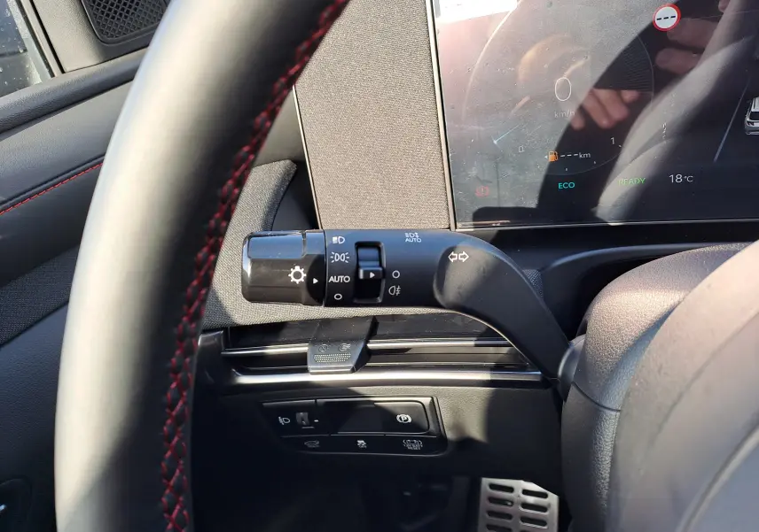 Vue intérieure côté gauche du volant du Hyundai Tucson 2025 noir, avec commandes d’éclairage et tableau de bord numérique.