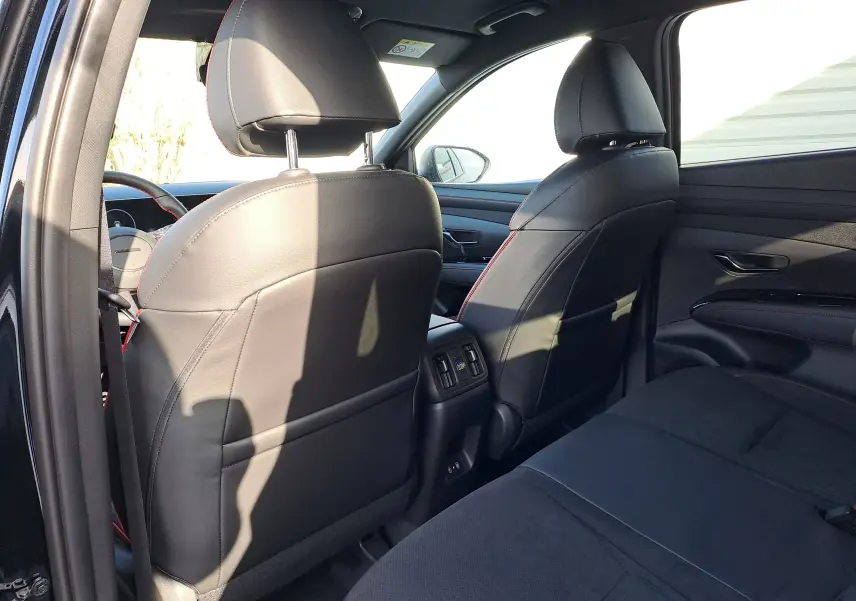 Vue intérieure arrière du Hyundai Tucson 2025 noir abyss, montrant les sièges avant en cuir noir avec surpiqûres rouges.