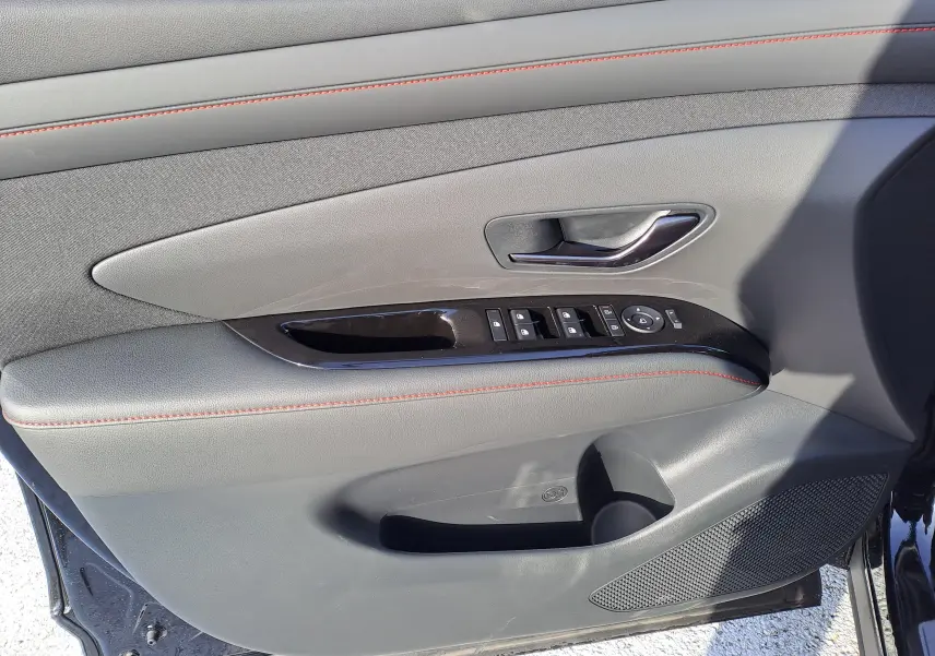 Vue rapprochée de la porte avant gauche du Hyundai Tucson 2025 noir abyss, avec surpiqûres rouges et commandes électriques.