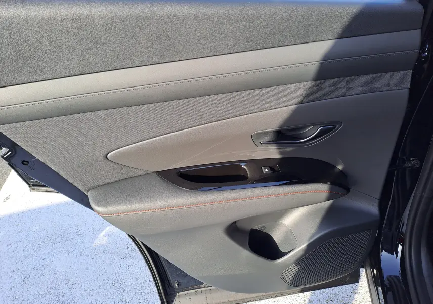 Vue intérieure de la porte arrière droite du Hyundai Tucson 2025 en Abyss Black, avec garniture grise et surpiqûres rouges.