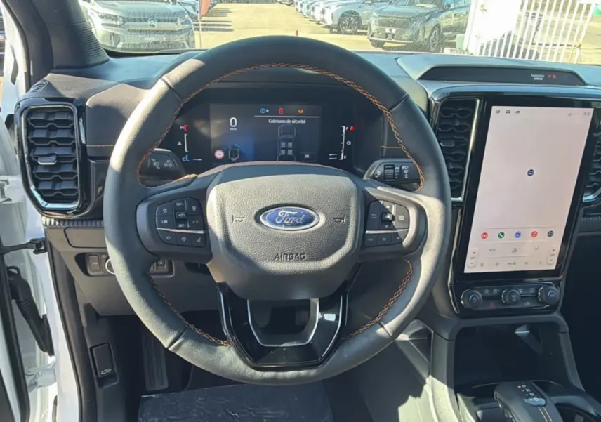 Vue intérieure frontale du volant cuir noir avec surpiqûres marron du Ford Ranger blanc, écran tactile vertical et tableau de bord digital.