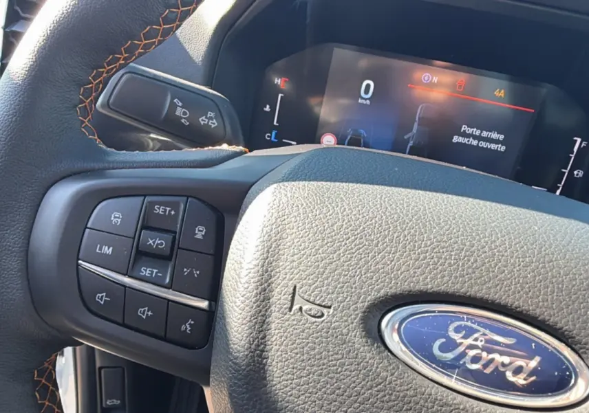 Gros plan sur le volant cuir noir avec surpiqûres orange et commandes multifonctions du Ford Ranger Wildtrak 2025.