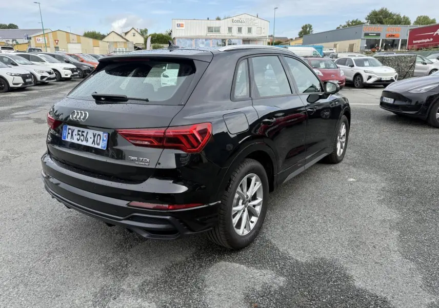 Audi Q3 noir vue 3/4 arrière droit sur parking, avec feux arrière LED et jantes aluminium 5 branches.