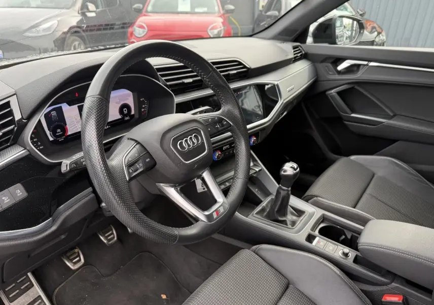 Intérieur noir de l'Audi Q3 S Line 2019, vue côté conducteur sur volant, levier manuel et tableau de bord numérique.