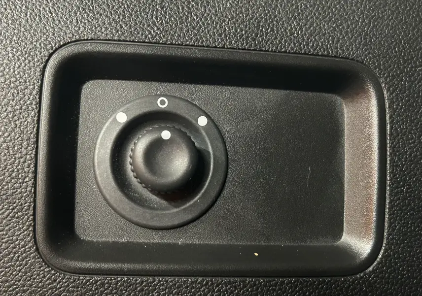 Gros plan sur le bouton de réglage des rétroviseurs noirs dans l’habitacle du Dacia Duster blanc 2023.