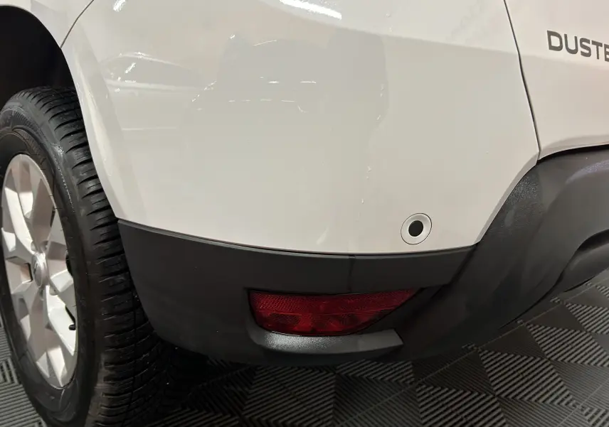 Gros plan sur l’arrière droit blanc du Dacia Duster 2023, avec feu antibrouillard et capteur de radar de recul.