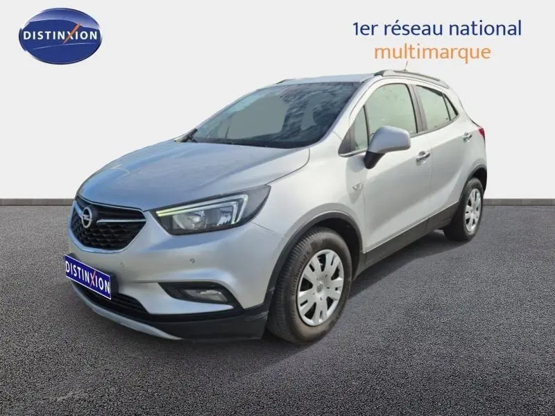 Opel Mokka X gris minéral vue 3/4 avant droit avec barres de toit et jantes acier.