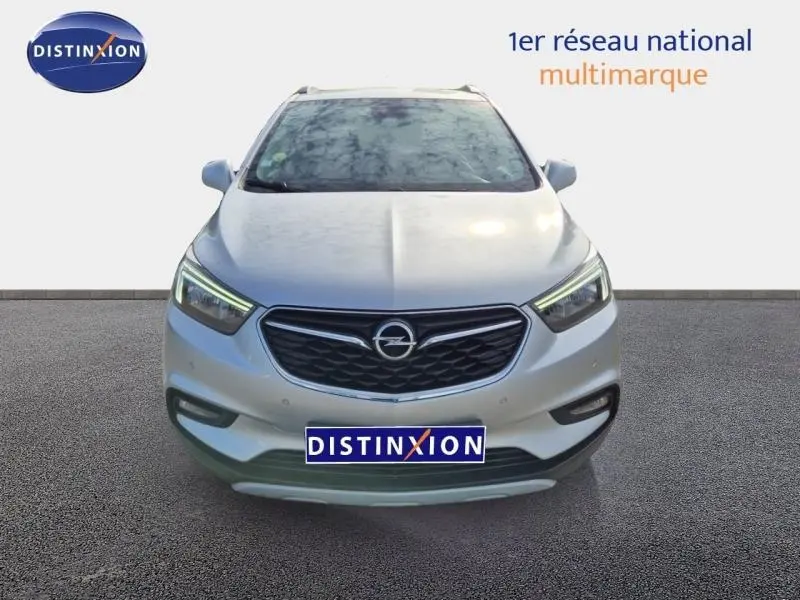 Vue avant d'un Opel Mokka X gris minéral avec calandre noire et feux LED allumés sur fond neutre.