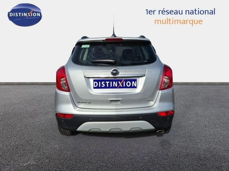 Vue arrière d'un Opel Mokka X gris minéral avec feux rouges et pare-chocs noir contrastant sur fond clair.