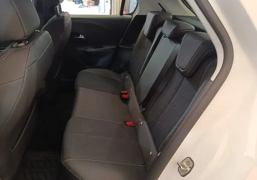 Vue intérieure côté arrière droit de l’Opel Corsa blanc, montrant la banquette arrière noire avec appuie-têtes et ceintures de sécurité rouges.