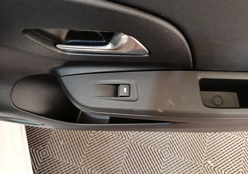 Gros plan sur la poignée intérieure et le bouton de verrouillage de la porte côté conducteur d'une Opel Corsa blanche.