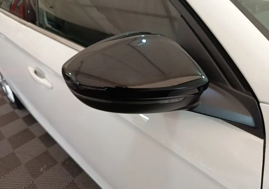 Gros plan sur le rétroviseur noir côté gauche d'une Opel Corsa blanche, avec porte et vitre partiellement visibles.