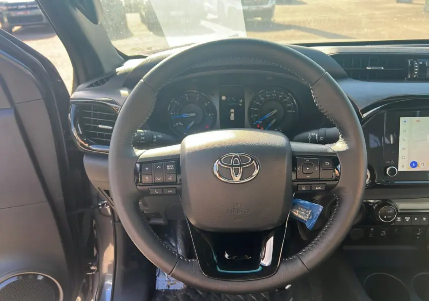 Vue intérieure centrée sur le volant du Toyota Hilux 2025, avec tableau de bord et écran tactile visibles.
