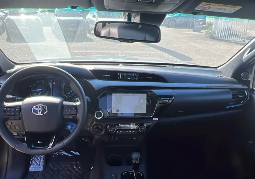 Vue intérieure avant du Toyota Hilux 2025 gris atlas, mettant en valeur le tableau de bord et l'écran tactile central.